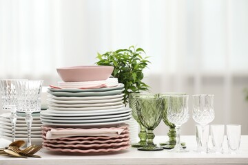 Clean glasses, plates, cutlery and green houseplant on white wooden table indoors