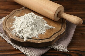Pile of flour and rolling pin on wooden table, closeup