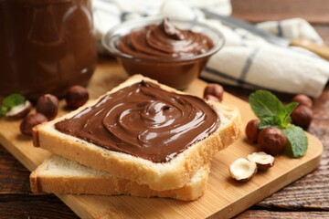 Toast with tasty chocolate hazelnut spread, nuts and mint on wooden table, closeup