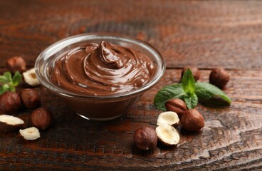 Chocolate hazelnut spread in bowl, nuts and mint on wooden table, closeup