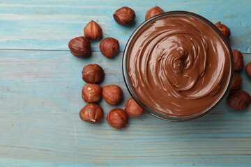 Chocolate hazelnut spread in bowl and nuts on light blue wooden table, flat lay. Space for text