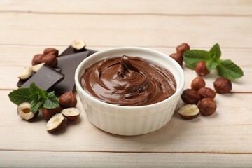 Chocolate hazelnut spread in bowl, nuts, pieces of chocolate and mint on wooden table, closeup