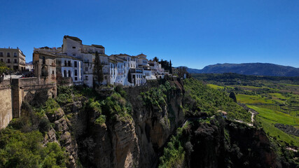 Fototapeta premium Ronda, Spain, white houses standing on cliff edge overlooking green valley landscape on sunny day