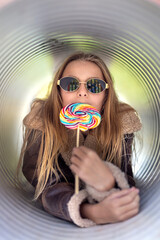 Happy pretty girl with lollipop in hand and sunglasses. Young woman with colorful candy at sunset in leather jacket