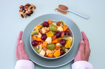 Female hands holding a green bowl full of fresh and colorful fruit. Apple, kiwi, orange, papaya, grape, mango, melon. Breakfast or break, healthy eating