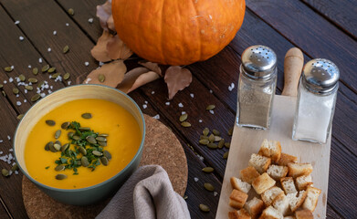 A pumpkin creamy soup in a bowl served with pumpkin seeds and croutons. Vegan soup. Dark wooden...