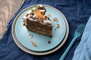 Slice of delicious carrot cake topped with cream cheese frosting, pecan pieces, and shaved carrot toppings.