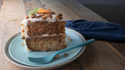 Slice of delicious carrot cake topped with cream cheese frosting, pecan pieces, and shaved carrot toppings.