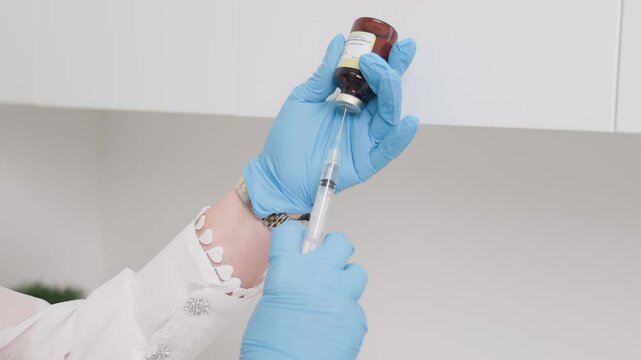 A close up of a medical practitioner with blue sterile gloves filling up a needle with solution