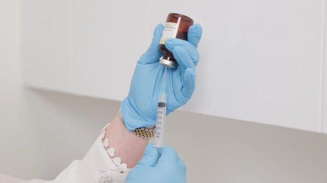 A close up of a medical practitioner with blue sterile gloves filling up a needle with solution