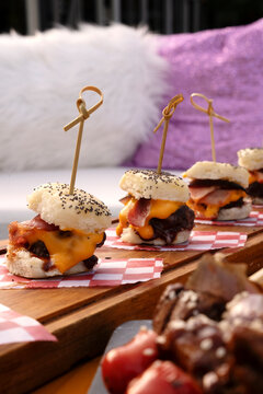 Social event catering. Closeup view of mini burgers with melted cheddar cheese and crispy bacon, presented in a wooden board