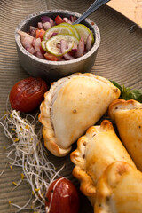 Hot finger food with a rustic presentation. Closeup view of gourmet traditional crispy meat empanadas with criolla sauce in a textured dish
