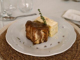 Fancy social event table arrangement and main course. Gourmet food. Closeup view of a pork loin with a soft cream sauce and potato mille feuille	
