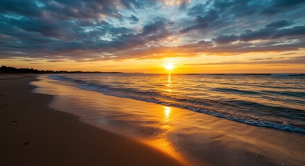 Obraz premium Wet sandy beach glowing under golden evening light and smooth ocean ripples.