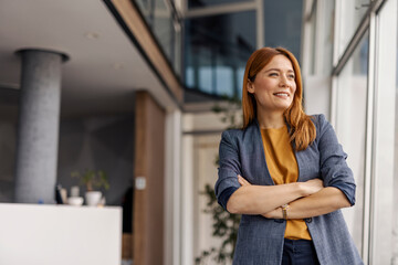 Portrait of successful female boss standing at corporation and looking through the window.