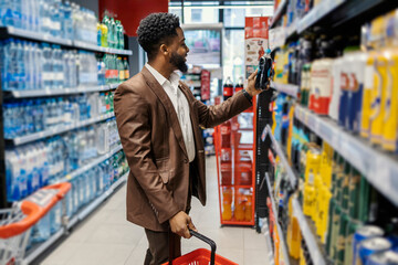 Side view of interracial man standing at supermarket and choosing bottle of juice.