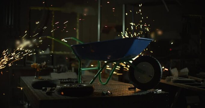 Wide, dolly in on silhouetted blue wheel barrow on metal shop table