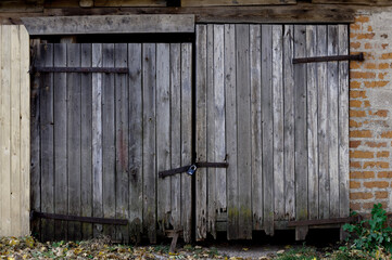 Old shed with closed half-rotten wooden gates with large rusty hinges and a padlock