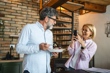 mature woman take a photo of man eating salad at home