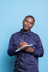 Security agent in safeguarding uniform takes notes on a notebook, standing against blue background....