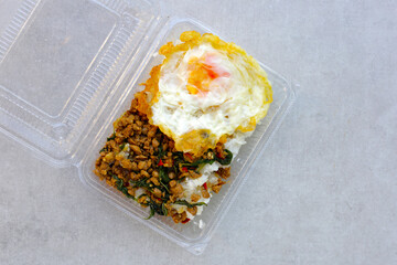 Stir-fried minced pork with holy basil served over jasmine rice, topped with a crispy fried egg, all packed neatly in a takeaway box
