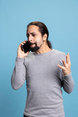 Furious young man getting mad and upset during a phone call with a friend, yelling and feeling...