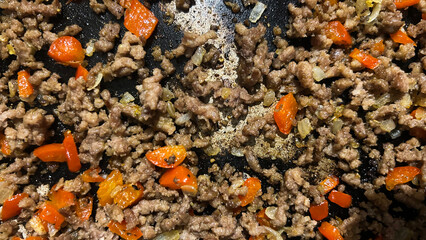 Ground meat and diced bell peppers cooking in a frying pan