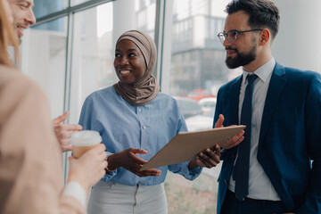Business people discussing work in office, holding a folder and drinking coffee