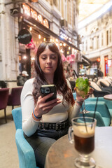 Young woman using smartphone and drinking cocktail in outdoor cafe