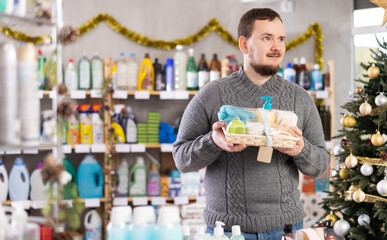 In Christmas decorated shop, man examines product and doubts, shower cosmetics present kit, study...