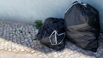 Two black garbage bags on a cobblestone street, waste management, urban cleanup, environment...