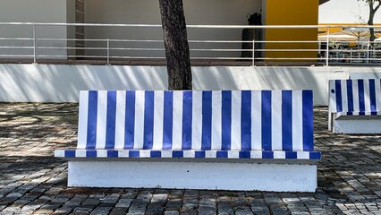 Blue and white striped bench under a tree, summer relaxation, outdoor leisure, travel destination,...
