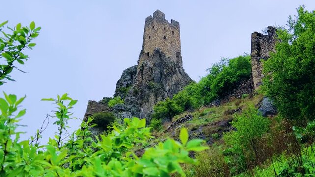 The tower complex is located inside the green mountains. The Republic of Ingushetia, Russia. View of the defensive towers of Ingushetia in the North Caucasus on a cloudy day in spring. 4K