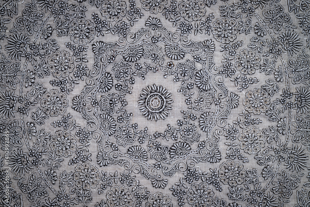 Poster detailed textile displays an array of floral and circular motifs in black on a gray background, show