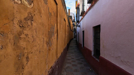 Narrow alley with colorful walls and tiled floor in Seville, Spain