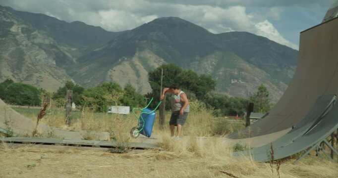 Funny guy playing with wheelbarrow on skating ramp - wide shot