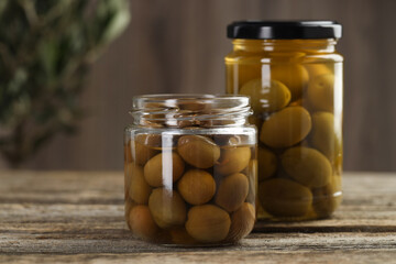 Pickled olives in glass jars on wooden table, closeup