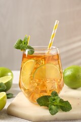 Refreshing iced tea with slices of lime, mint and drinking straw in glass on light textured table against grey background, closeup