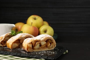 Pieces of tasty apple strudel with powdered sugar and mint on black table, closeup. Space for text
