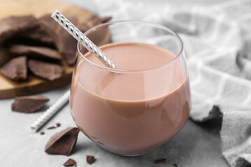 Tasty chocolate milk in glass and pieces of chocolate on light grey table, closeup