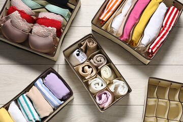 Organizers with folded clothes and underwear on wooden floor, flat lay
