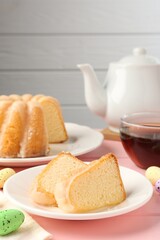 Pieces of delicious bundt cake, Easter eggs and tea on pink wooden table