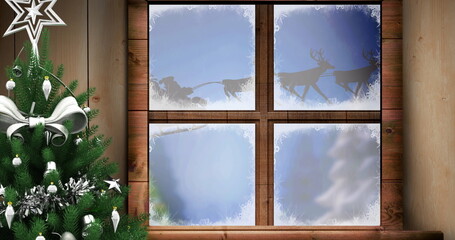 Image of santa claus in sleigh with reindeer seen through window and christmas tree