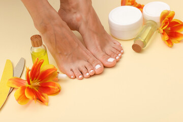 Pedicure. Woman showing toenails covered with nail polish, flowers, tools and cosmetic products on beige background, closeup