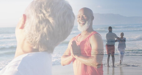 Composite of happy diverse senior couple doing yoga, and dancing on beach © vectorfusionart