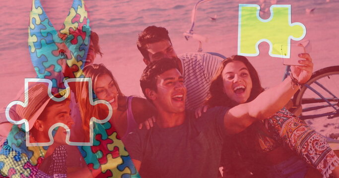 Image of colourful puzzle pieces ribbon over happy friends taking selfies at summer beach party