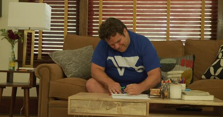 Happy man in wheelbarrow shirt coloring in living room, steady cam shot