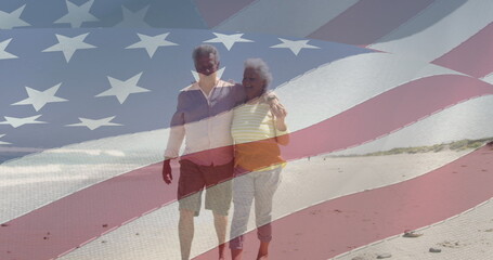 Image of happy senior caucasian couple embracing on beach over flag of united states of america