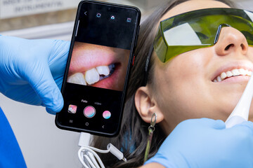Patient watches real-time dental scan on phone during a modern intraoral examination with dentist in blue scrubs