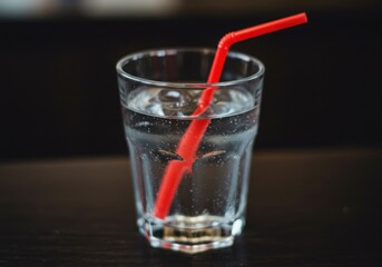 A glass of water with a red straw inside sitting on a dark surface in a simple still life shot
